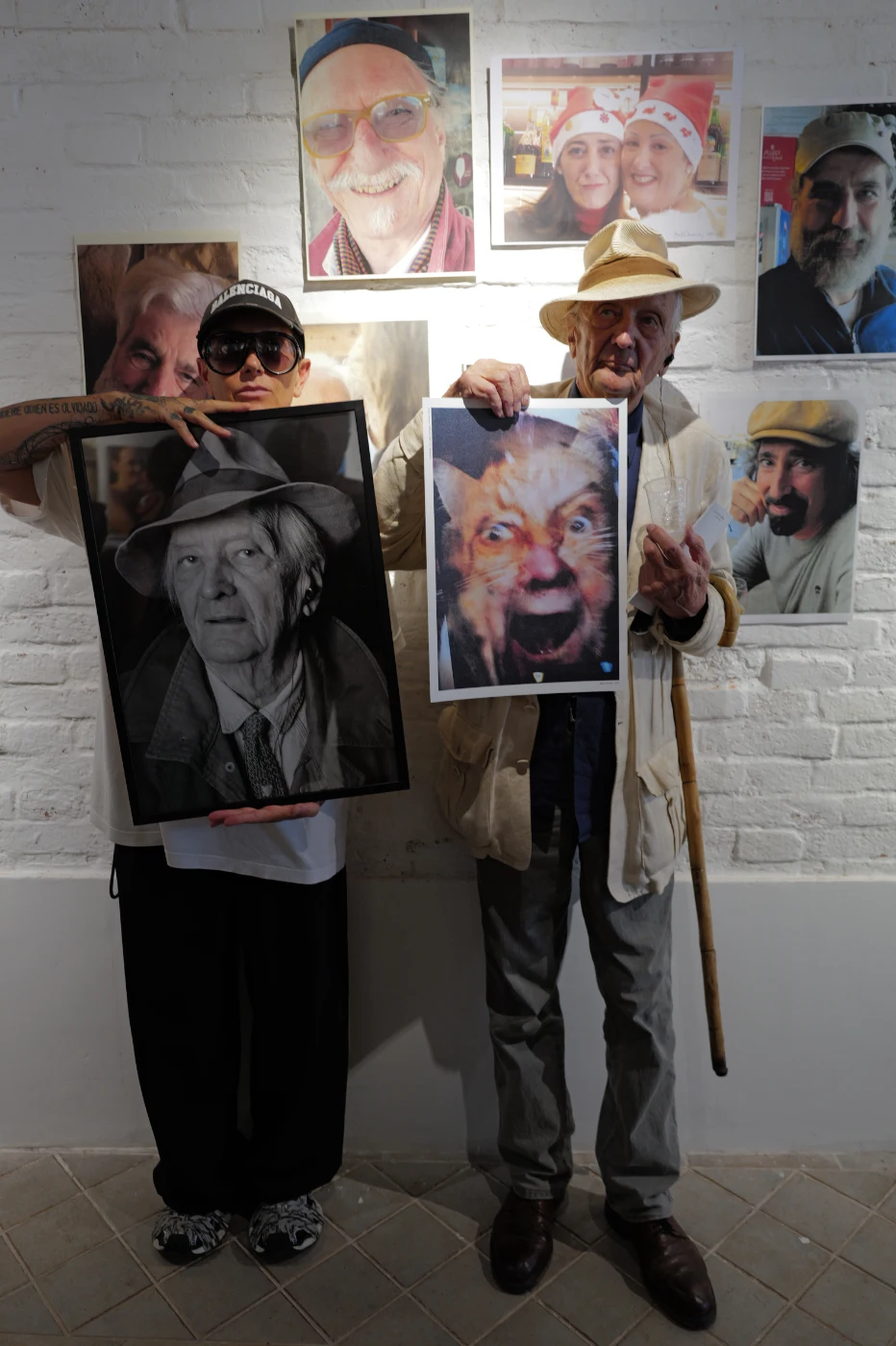 Italo Zannier and Barbara Pigazzi holding his portrait and his cat self-portrait at the exhibition